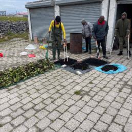 Volunteer in a yellow crewneck and boots working with tools on drying water hyacinth for conservation efforts.