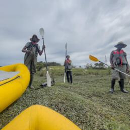 Three volunteers standing alongside two yellow canoes on the shore, preparing for a community water activity.