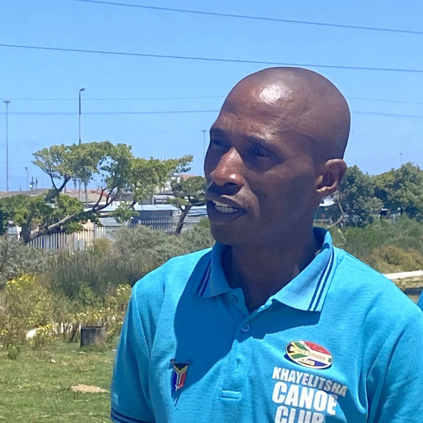 Black man in a blue polo with an official South Africa tour guide badge, leading a tour in Khayelitsha.